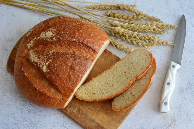 pan fresco en tabla de cortar con rebanadas de pan, cuchillo y espigas de trigo