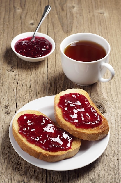 Pan frito con mermelada y taza de té en la mesa de madera antigua