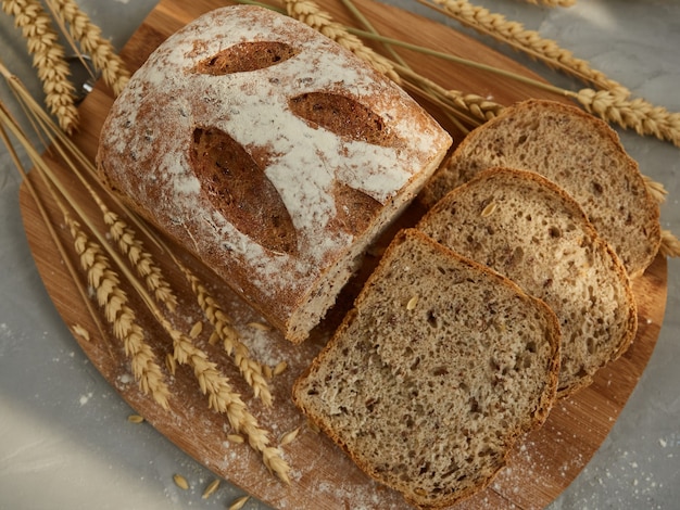 Pan de grano en rodajas, sobre una tabla de madera con espigas y granos