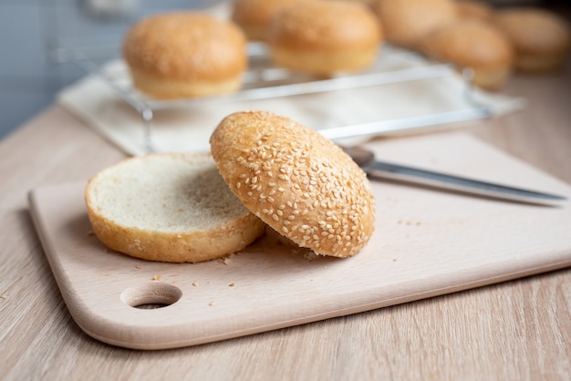 Foto pan de hamburguesa de sésamo cortado por la mitad en una tabla en la cocina