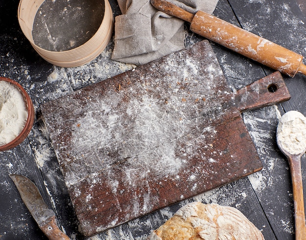 Pan, harina de trigo blanca, rodillo de madera y tabla de cortar vieja.