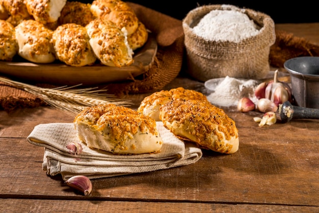 Pan hecho con ajo sobre tela sobre mesa rústica de madera con otros panes, ajo y harina al fondo.