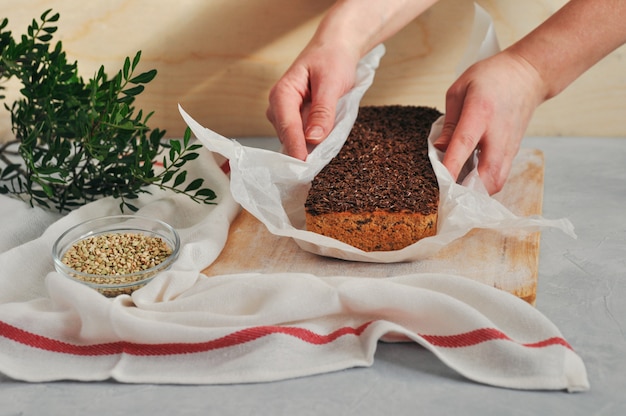 Foto pan hecho en casa de un vegano en una levadura del alforfón verde con las semillas de lino, girasol en las manos de las mujeres en un fondo de madera. nutrición sana y adecuada.