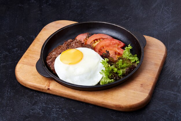 Pan con huevo frito, rodajas de tomate, ensalada y chuleta