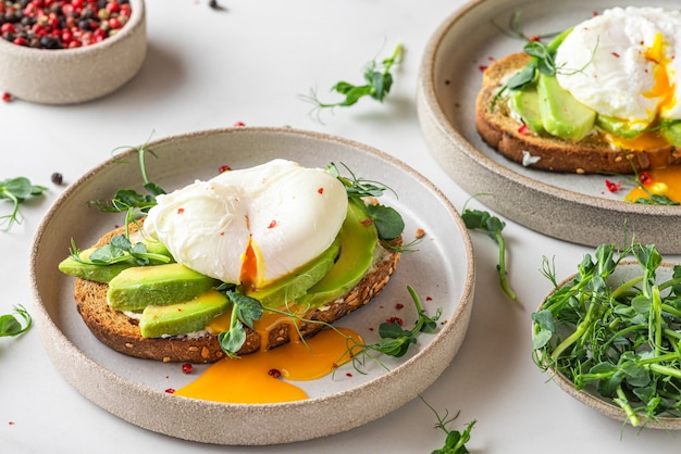 Pan integral tostado con aguacate, huevo poché, queso tierno y brotes sobre blanco