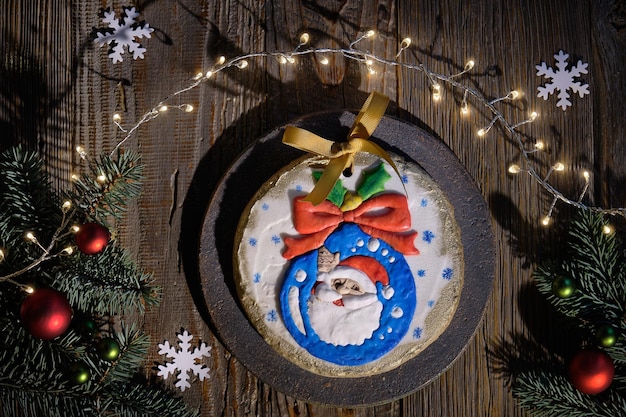 Pan de jengibre ornamentado decorado con Papá Noel sonriendo desde la chuchería de Navidad. dos personajes de vaca de dibujos animados. El piso de Navidad yacía con ramitas de abeto, adornos rojos, copos de nieve de papel. Vista superior, fondo de madera rústica oscura.