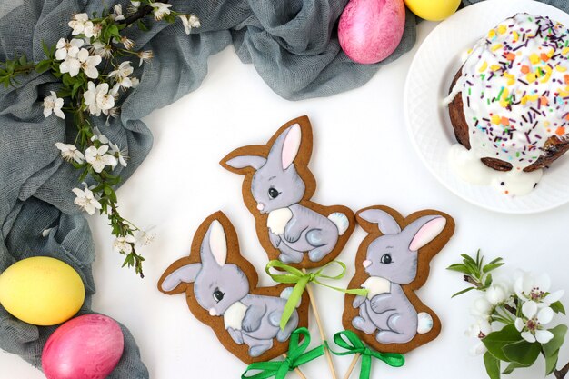 Pan de jengibre de Pascua en forma de lindos conejos en palos ubicados sobre un fondo blanco, vista superior