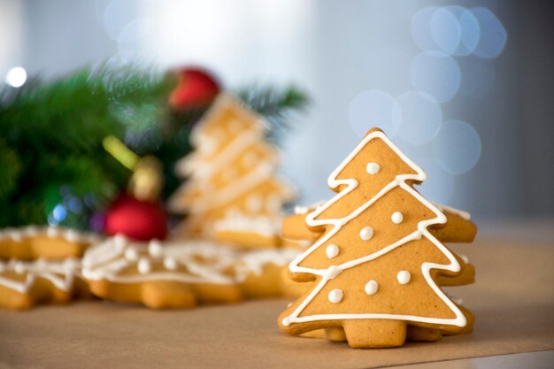 Pan de jengibre tradicional en forma de árbol de Navidad con glaseado blanco y ramas de abeto juguetes rojos y luces bokeh de fondo