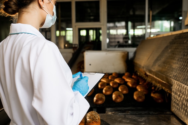 Un pan. Línea de producción de pan. Mujer en uniforme. Control sanitario.