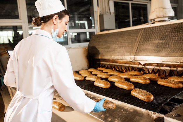 Un pan. Línea de producción de pan. Mujer en uniforme. Control sanitario.