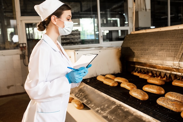 Un pan. Línea de producción de pan. Mujer en uniforme. Control sanitario.