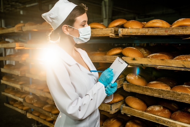 Un pan. Línea de producción de pan. Mujer en uniforme. Control sanitario.