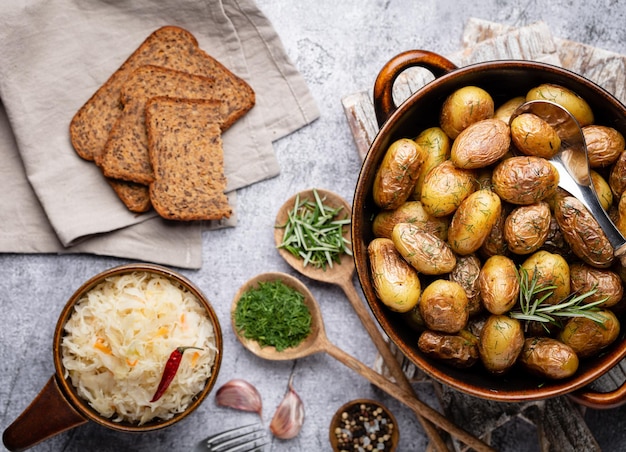 Pan lleno de papas asadas rodadas sobre una mesa rústica de madera. Los ingredientes que incluye son patatas crudas, romero, eneldo, sal, pimienta y ajo.