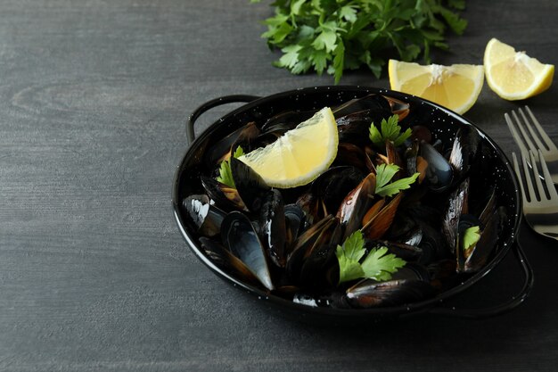 Pan con mejillones frescos sobre mesa de madera oscura.