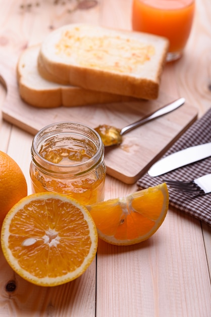 Pan con mermelada de naranja y jugo de naranja en la mesa de madera.