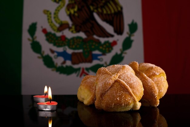 Pan de muerto y velas sobre una mesa de cristal negro con bandera mexicana al fondo Día de los muertos dess