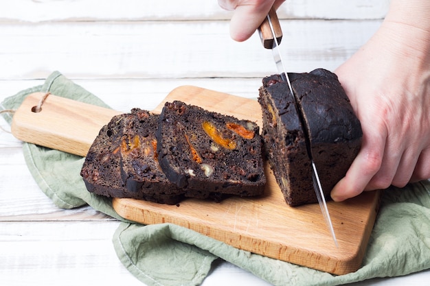 El pan negro de postre dulce con ciruelas, albaricoques y nueces se corta con un cuchillo de cocina.