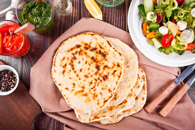 Pan plano naan indio casero con ensalada fresca y salsas en la mesa de la cena