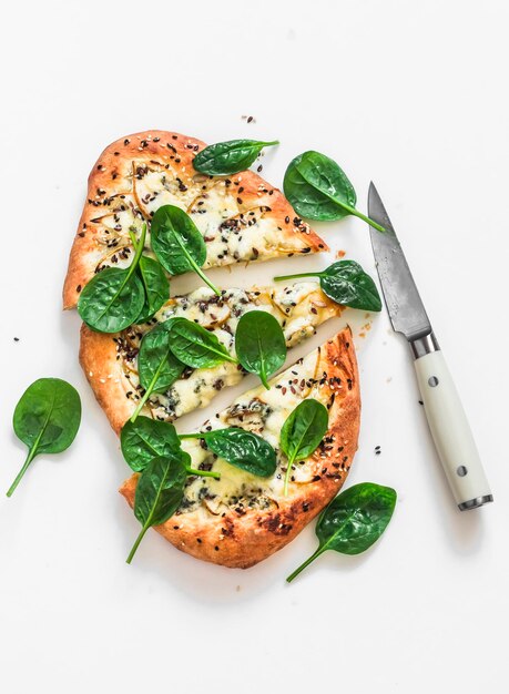 Foto pan plano con queso azul, pera, sésamo y espinacas frescas en una vista superior de fondo claro