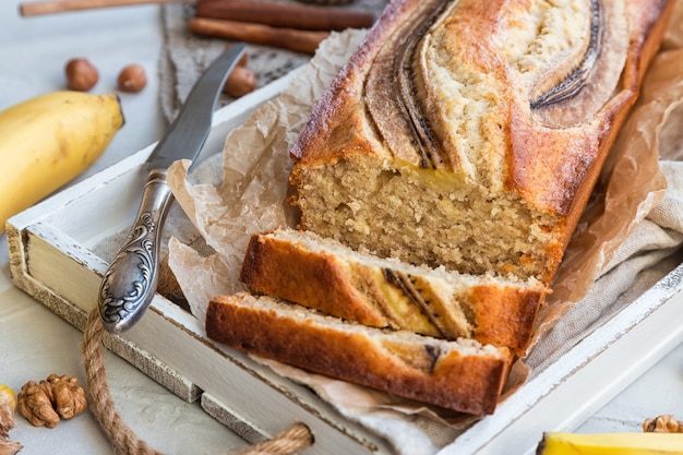 Pan de plátano casero fresco en bandeja de madera blanca con ingredientes en hormigón ligero