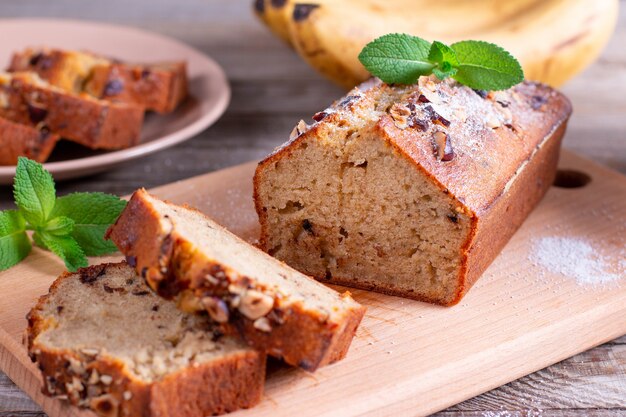 Pan de plátano con plátanos en rodajas sobre una tabla de cortar de madera con plátanos en segundo plano.