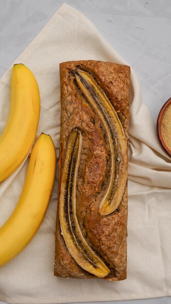 el pan de plátano rodeado de plátanos frescos e ingredientes para cocinar se encuentra sobre un fondo gris claro