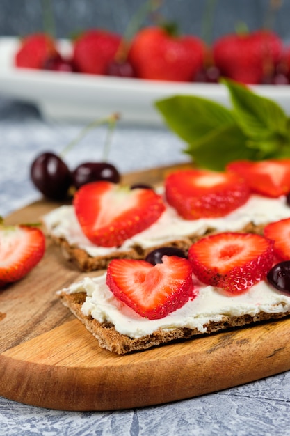 Pan con queso cottage, fresas frescas y cerezas en una tabla de madera