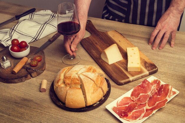 Pan queso y jamón en una mesa de madera y un hombre con una copa de vino tinto