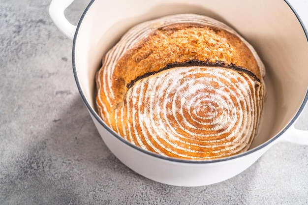 Pan recién horneado de pan de masa fermentada de trigo con marcas de una cesta de prueba de pan en un horno holandés de hierro fundido esmaltado.