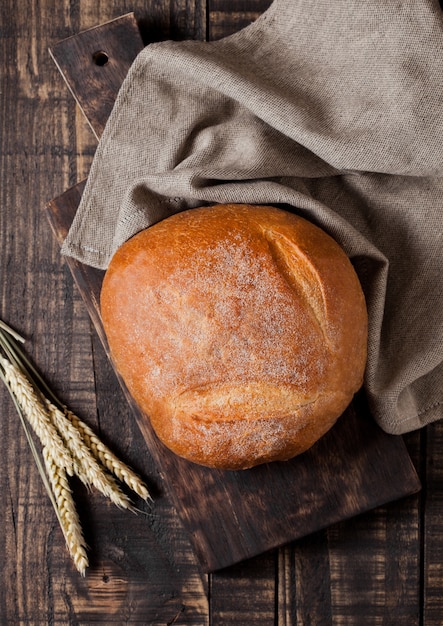 Pan recién horneado con papel de cocina y trigo sobre tabla de madera oscura