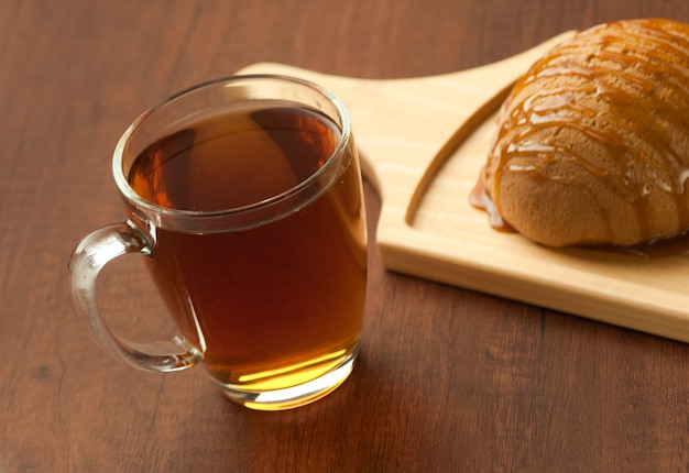 Pan rociado con miel en una placa de madera y una taza de té negro