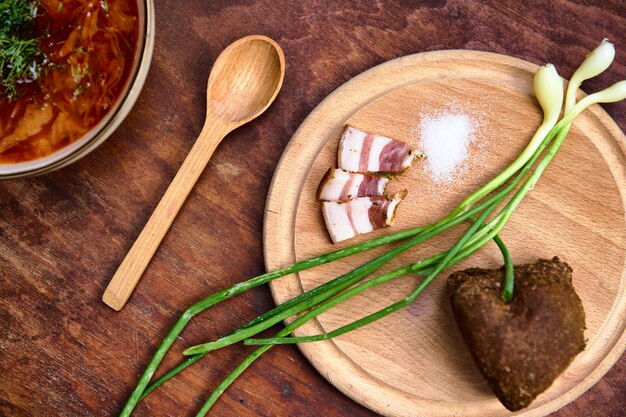 Pan de sal de tocino en rodajas y cebolla verde en una tabla de madera cerca de una cuchara de sopa Vista parcial del plato ucraniano Borscht