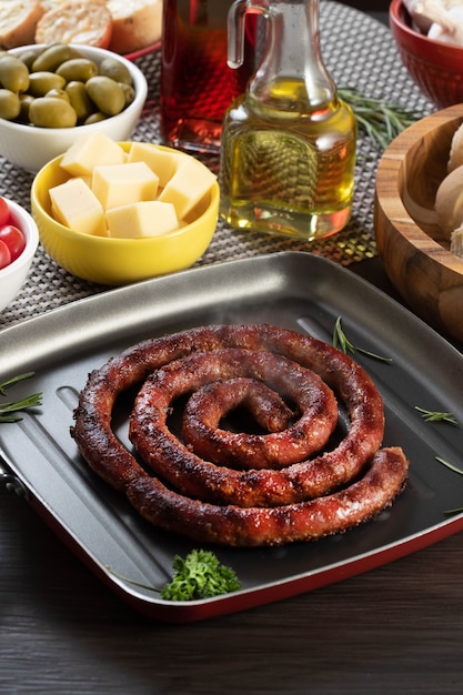 Pan de salchicha y ajo en un plato rojo sobre la mesa de barbacoa con aperitivos, queso, romero, aceitunas y tomates cherry.