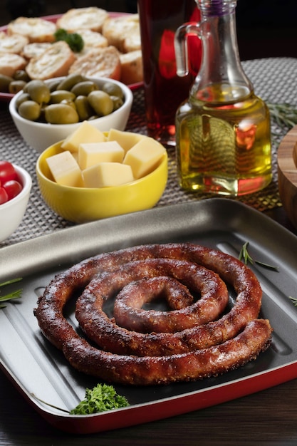 Pan de salchicha y ajo en un plato rojo sobre la mesa de barbacoa con aperitivos, queso, romero, aceitunas y tomates cherry.