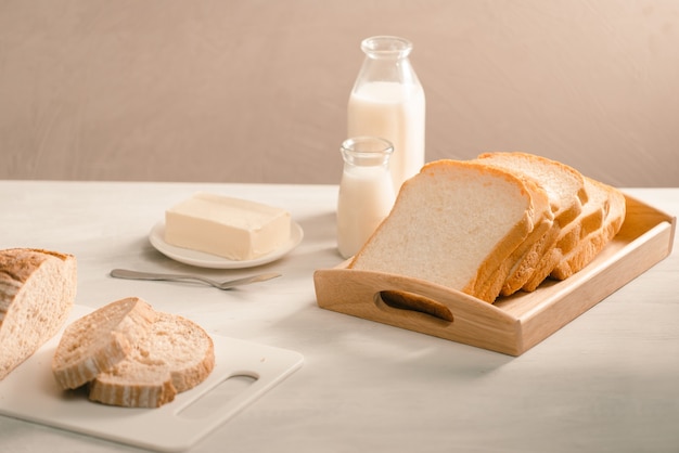 Pan en el soporte de la placa rodeado de mantequilla y leche en primer plano de la mesa blanca