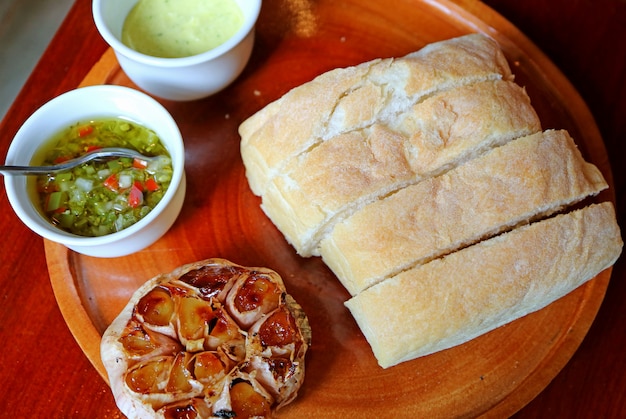 Foto pan suave al horno y ajo asado con dips en una placa de madera