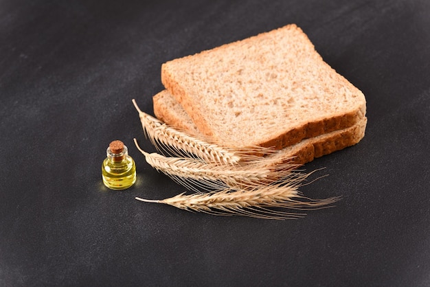 Pan tostado crudo con espigas de trigo y una botella de aceite sobre fondo oscuro