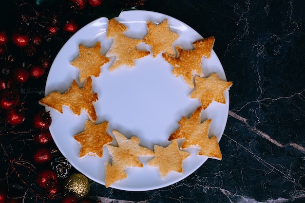 Pan tostado en forma de árbol de Navidad y estrellas se encuentran en un plato blanco, primer plano. Enfoque selectivo.