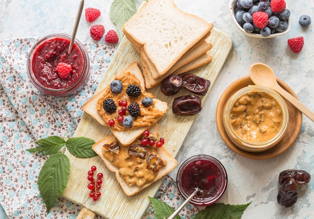 Pan tostado con mermelada de fresa casera y mantequilla de maní servido con bayas. Pan tostado casero con mermelada y mantequilla de maní en la mesa de madera para el desayuno.