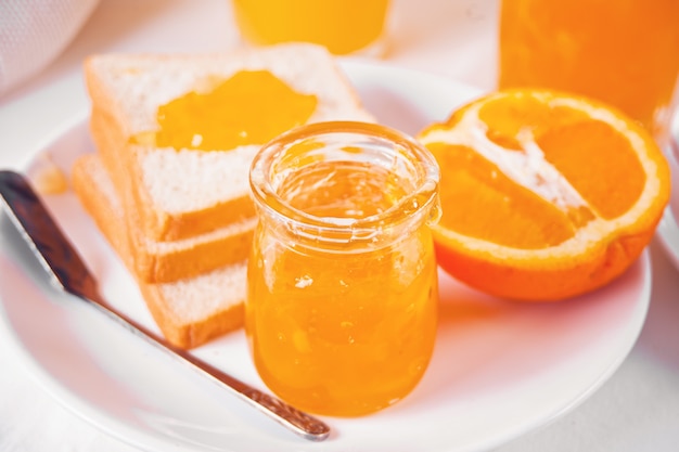 Pan tostado con mermelada de naranja, vasos de jugo de naranja sobre la mesa blanca. Concepto de desayuno.