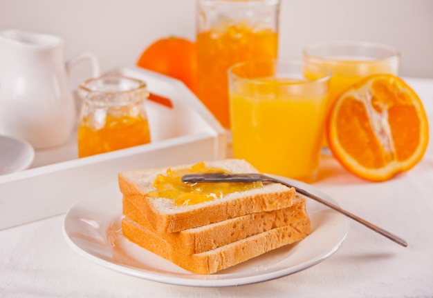 Pan tostado con mermelada de naranja, vasos de jugo de naranja en la superficie blanca Concepto de desayuno.
