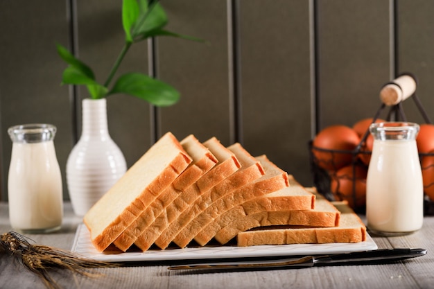 Pan tostado en rodajas de pan blanco (Shokupan o Roti Tawar) para el desayuno sobre fondo de madera, servido con huevo y leche. Imagen del concepto de panadería