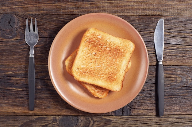 Pan tostado, tenedor y cuchillo en la mesa de madera oscura, vista superior