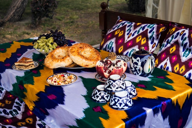 Pan tradicional uzbeko en la mesa con tazas y tetera Cocina de Asia Central frutas uvas y granada y dulces en platos