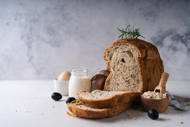 Pan de trigo integral casero en rodajas frescas con aceite de oliva sobre fondo rústico blanco