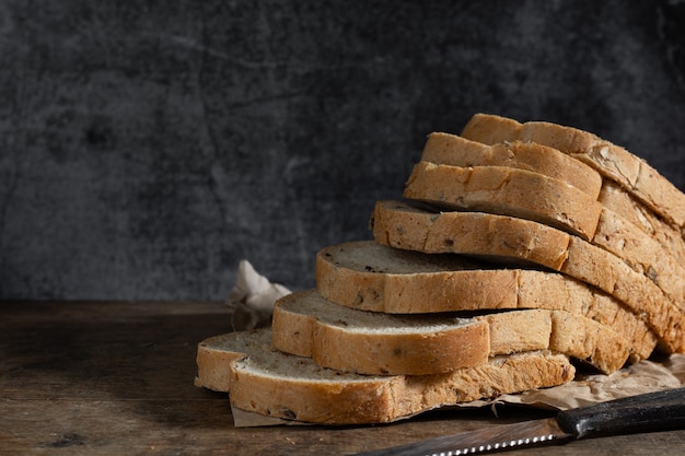 Pan de trigo integral de grano en rodajas sobre fondo oscuro de madera rústica, ingredientes bio, comida sana.