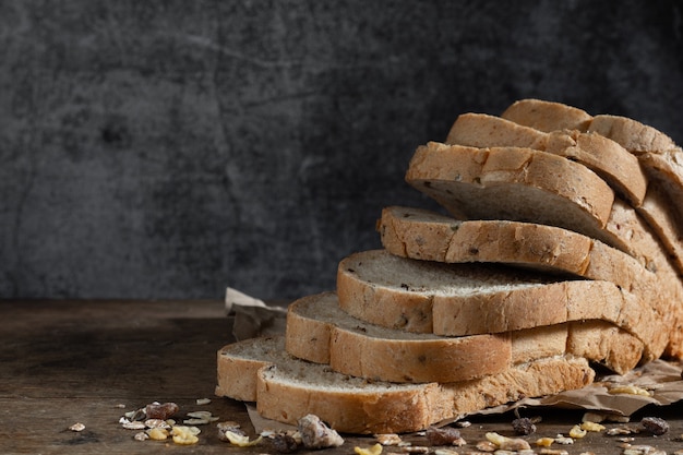 Pan de trigo integral de grano en rodajas sobre fondo oscuro de madera rústica, ingredientes bio, comida sana.