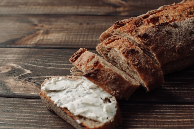 Pan de trigo sarraceno oscuro con sisam cubierto con queso cottage con hierbas en un corte sobre una mesa de madera en un estilo rústico.