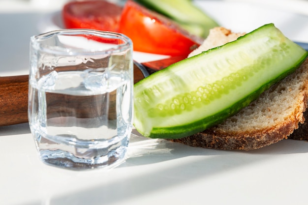 Pan, verduras y un vaso de vodka en la mesa. Aperitivo fresco de pepino y tomate. De cerca.