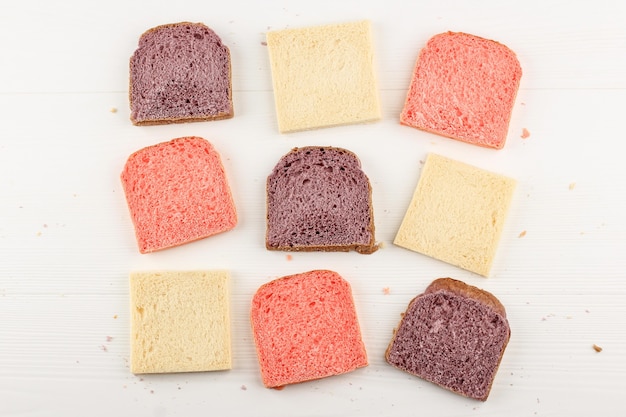 Pan de vista superior rosa, blanco y morado para el desayuno de sándwich. Aislado en el fondo de madera blanca. Concepto de panadería limpia